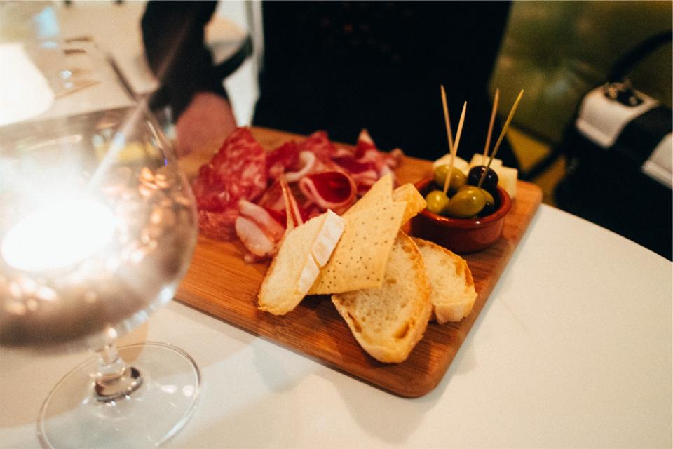 wine toothpicks olives glass food eating cuttingboard curedmeat coldcuts cheese bread appetizers 