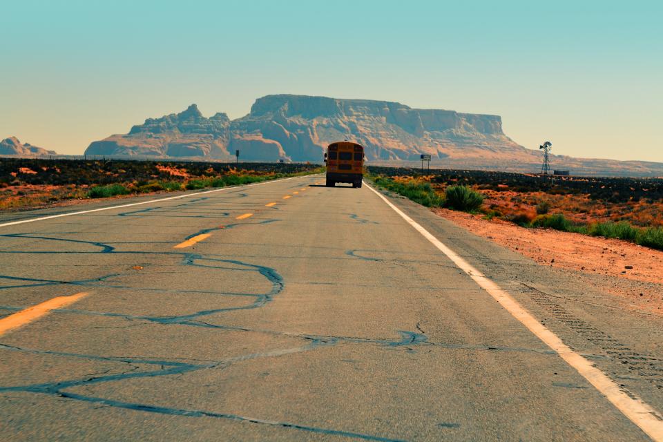 sunshine schoolbus sand rural road plants pavement mountains hot desert cliffs 