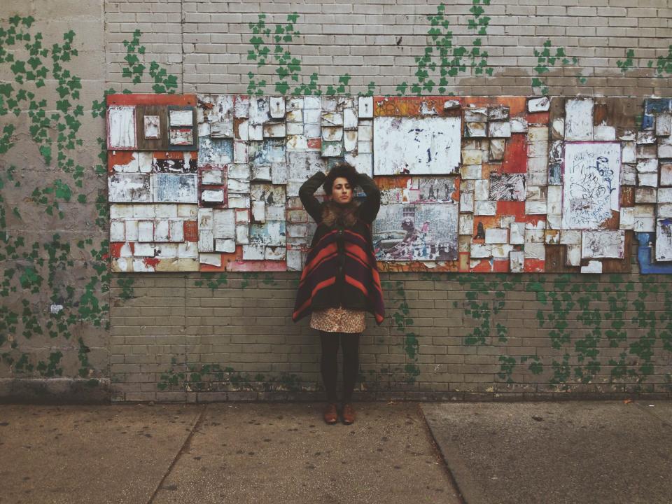 woman wall sidewalk people papers jacket girl dress Coat bulletins bricks boards 
