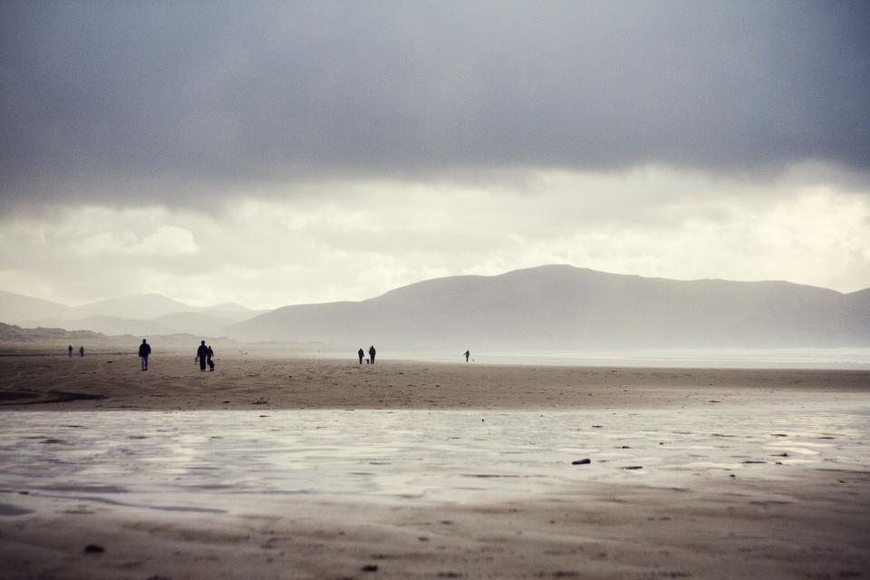 water sky sand people mountains hills grey clouds beach 