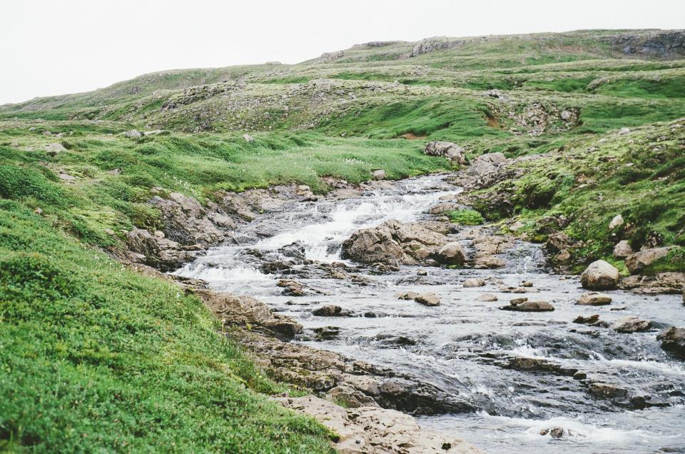 water stream rocks river hills green grass fields 