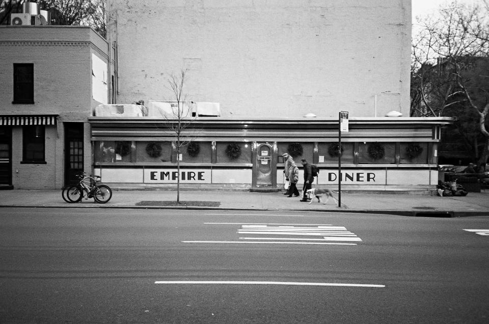 walking street road restaurant people pedestrians food dog diner city busstop buildings blackandwhite bikes bicycles animal 