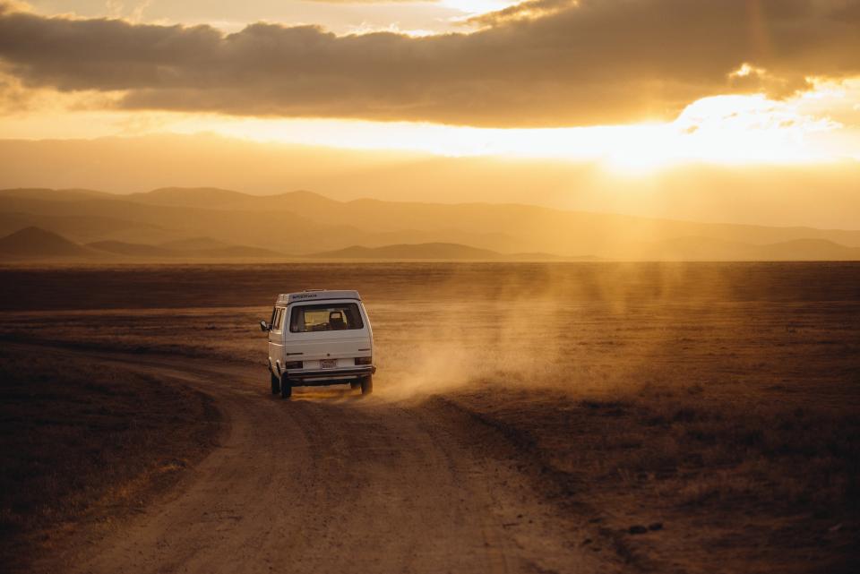 white van tires sunshine sunset sunrays sky road mountains dirt desert clouds 