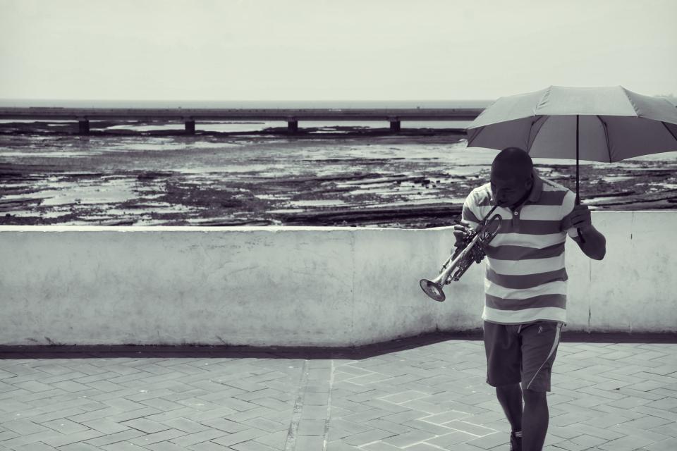 water umbrella trumpet shorts sea people Panama ocean musician music man guy blackandwhite 