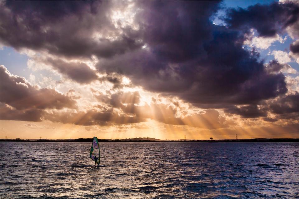windsurfing water sunset sunbeams sky sea ocean clouds 