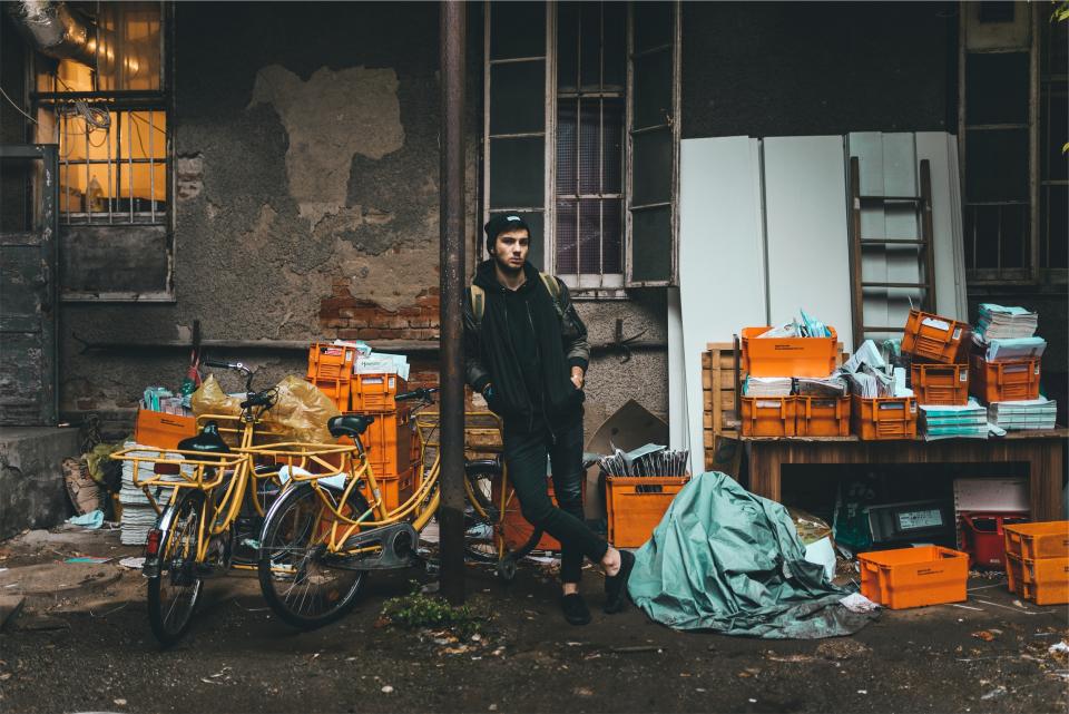 alley, concrete, crates, boxes, papers, magazines, bikes, bicycles, young, guy, hat, toque, beanie, backpack, jacket, jeans, denim, clothes, fashion, model, urban, people