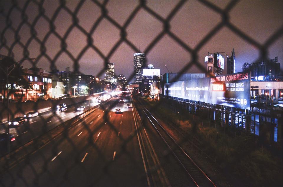 road overpass night lights highway fence evening dark city chainlink cars buildings billboards 