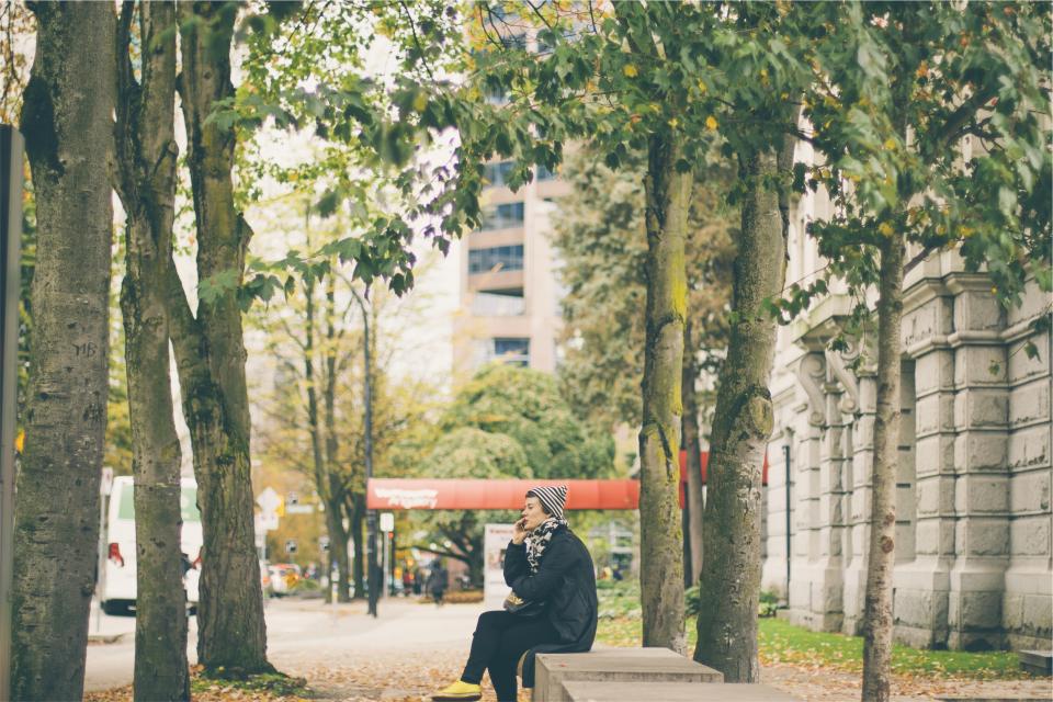 woman trees talking street sitting sidewalk people jacket hat city cellphone bench 